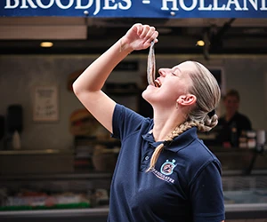 Medewerker van ZeeYouLater Visspecialist met een Hollands Nieuwe haring in de viskraam in Nijkerk